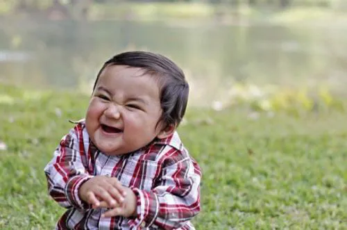 a young boy sitting on the grass next to a lake .png